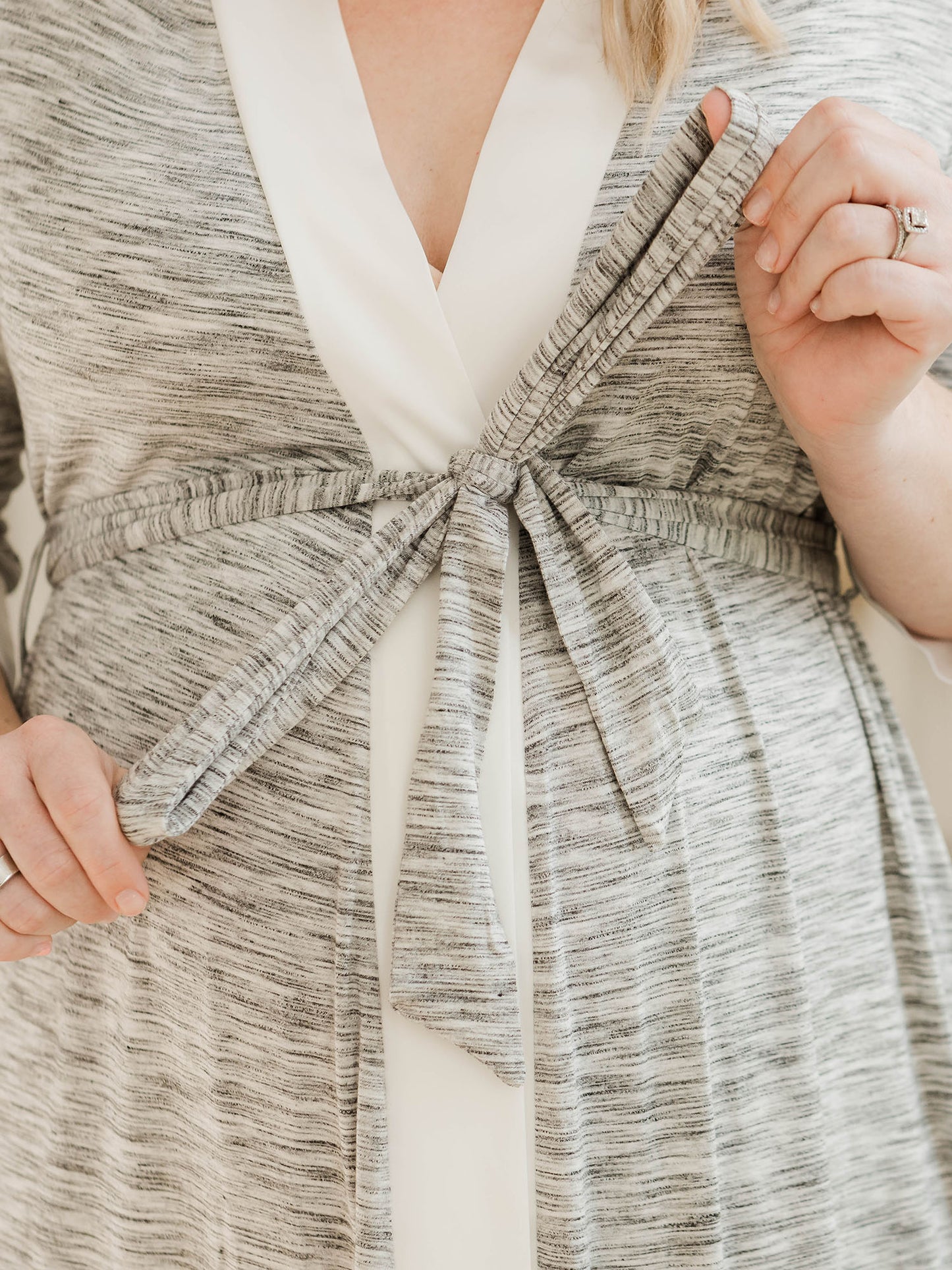 Closeup of a pregnant model wearing the Emmaline Robe in Grey with her thumbs hooked into the tie