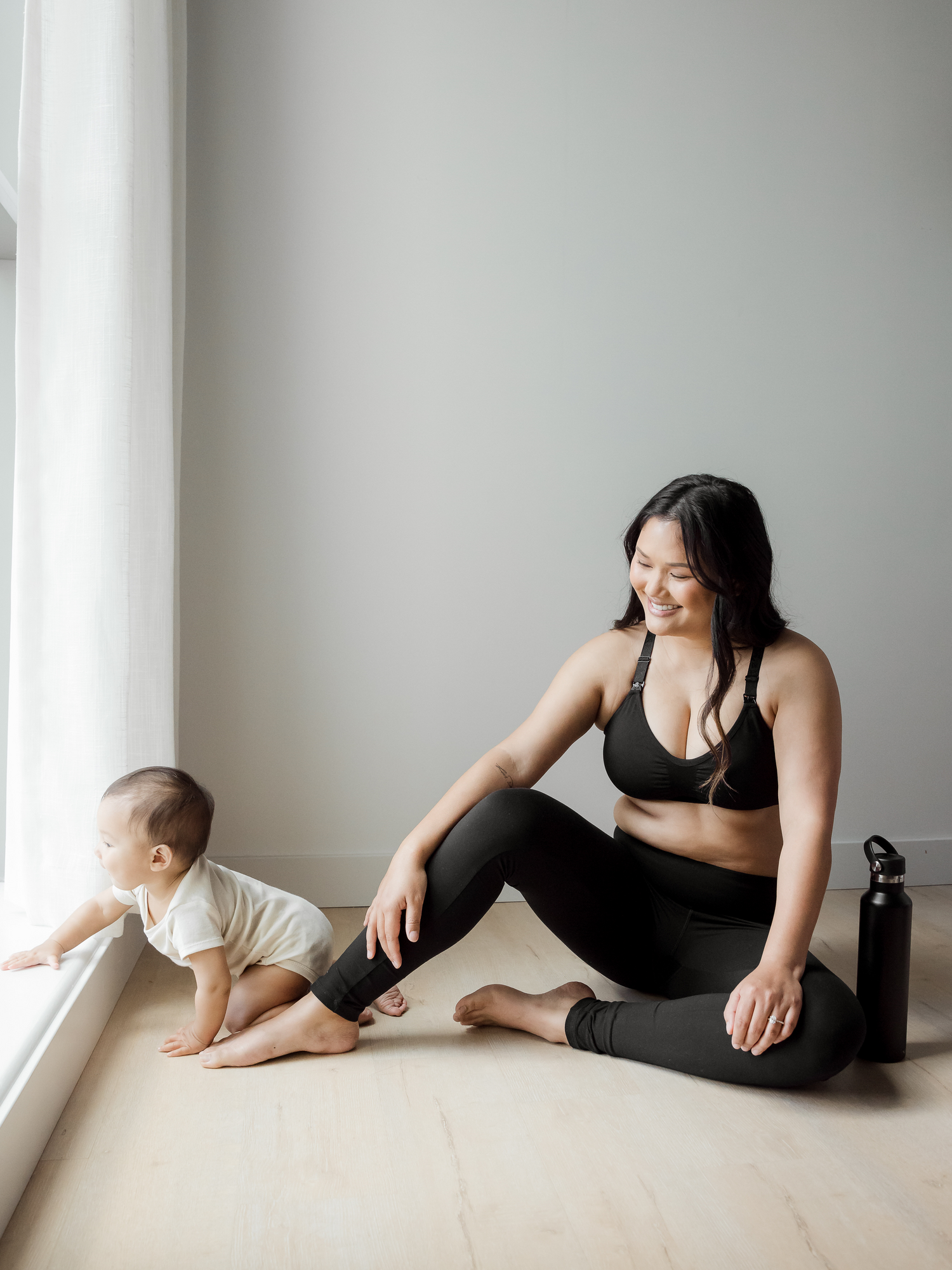 Model sitting on the ground with her baby wearing the Louisa Maternity & Postpartum Legging in black with pockets. @model_info:Binc is 5'5" and wearing a Medium. 