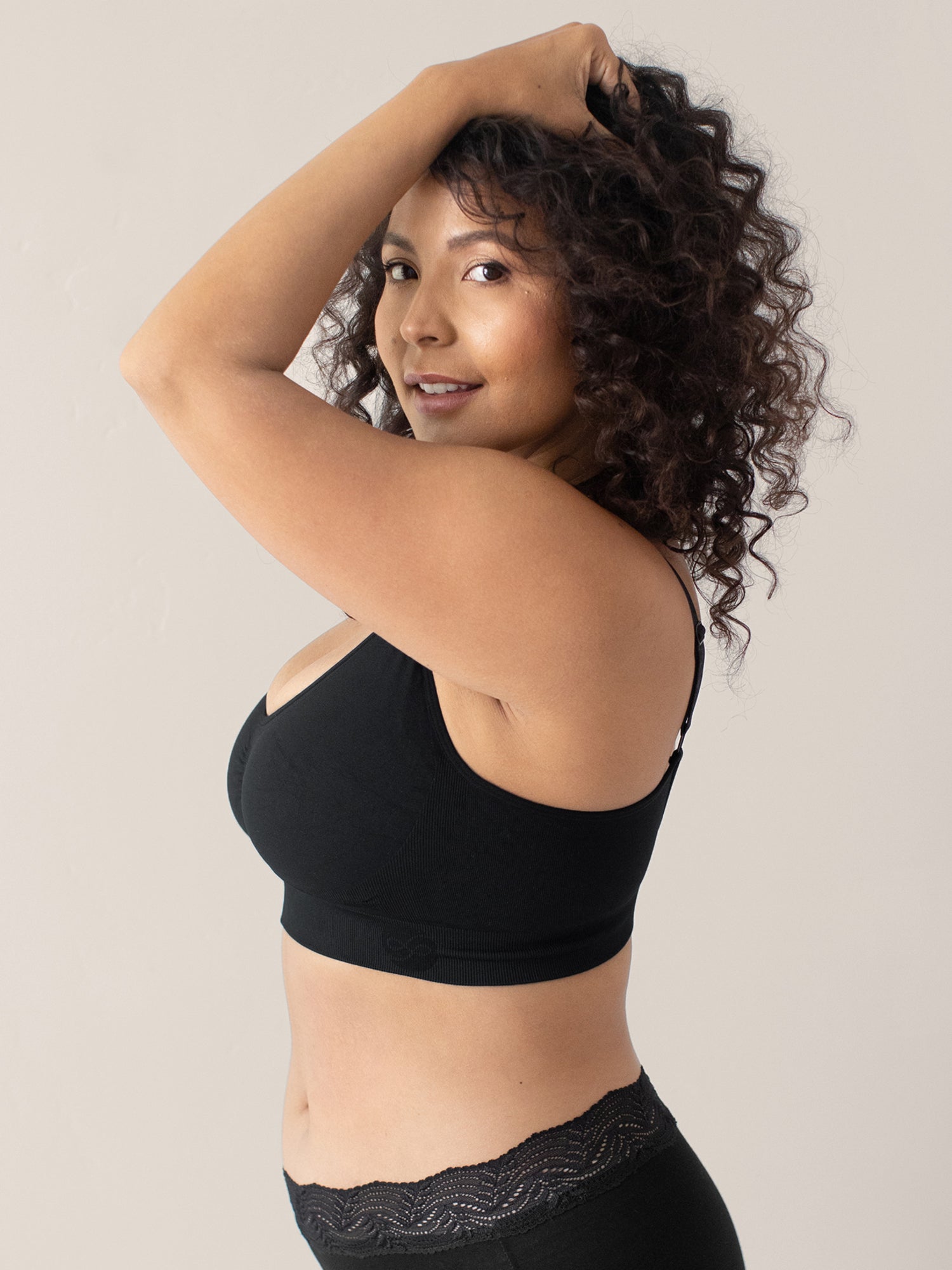 Side view of a model wearing the Nellie Sublime® Wireless Bra in Black with her hands in her hair @model_info:Sierra is wearing a Medium Busty.