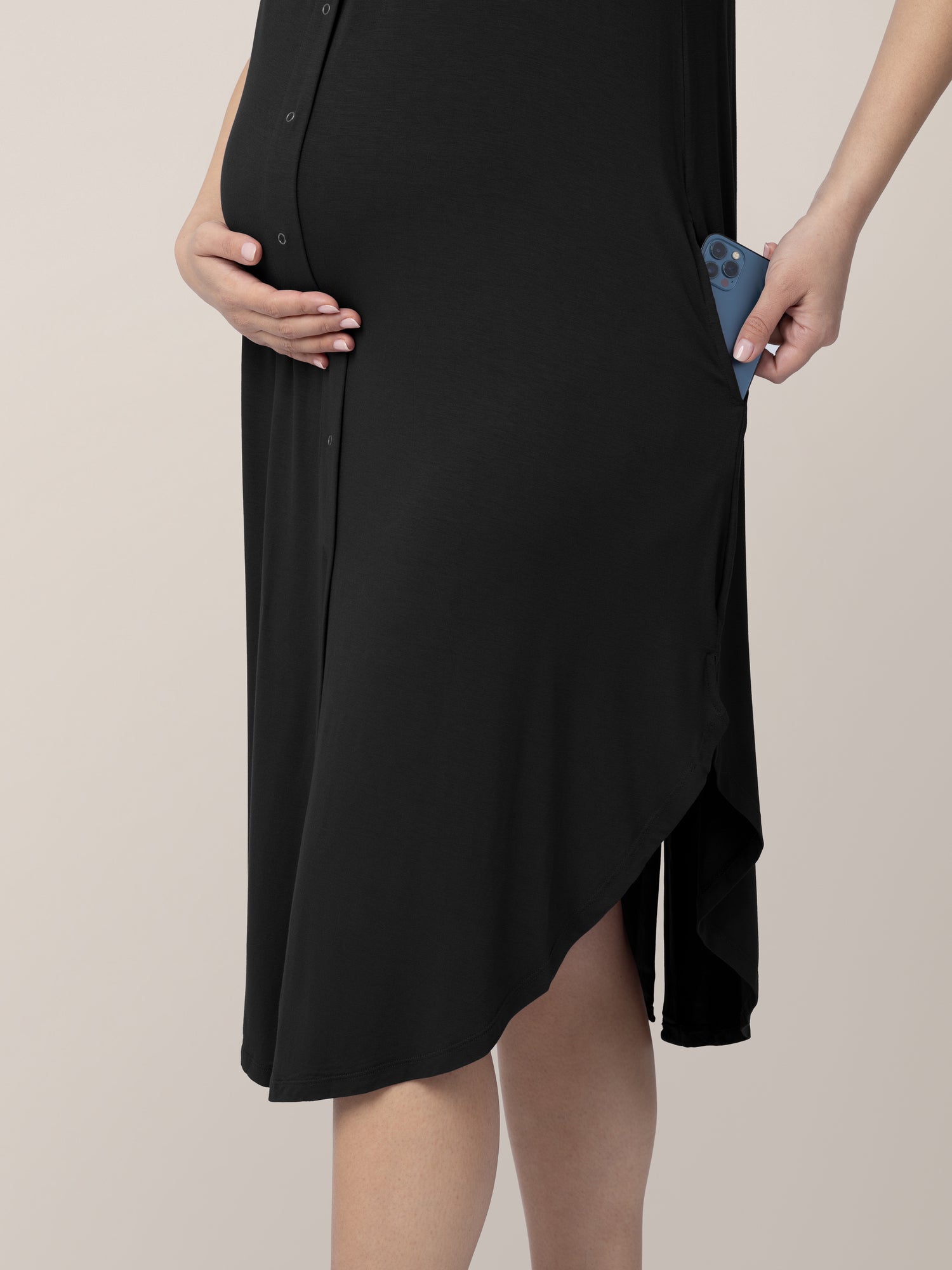 Pregnant model wearing the Ruffle Strap Labor & Delivery Gown in Black showing her phone in the side pocket.