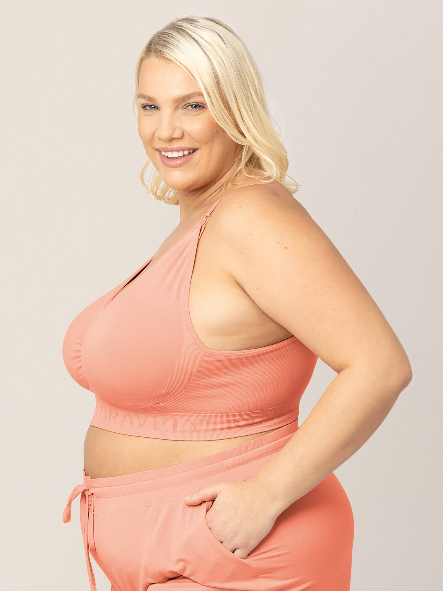 Side view of a model wearing g the Simply Sublime® Nursing Bra in Vintage Coral with her hands in her pockets. 