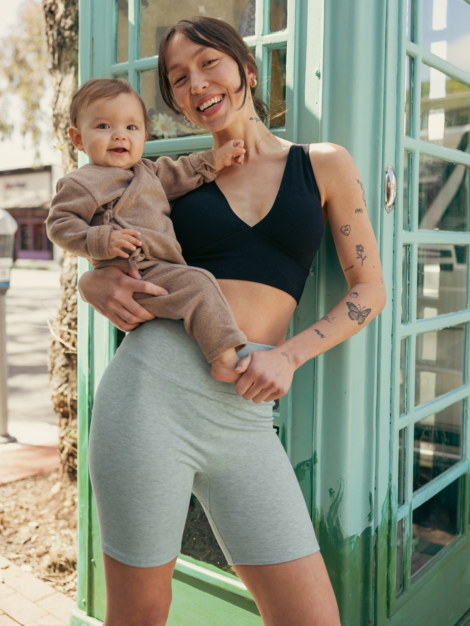 Model holding baby and wearing the Sublime® Bamboo Maternity & Postpartum Bike Short in dusty blue green heather. @model_info:Lyn is 5'6" and wearing a Small.