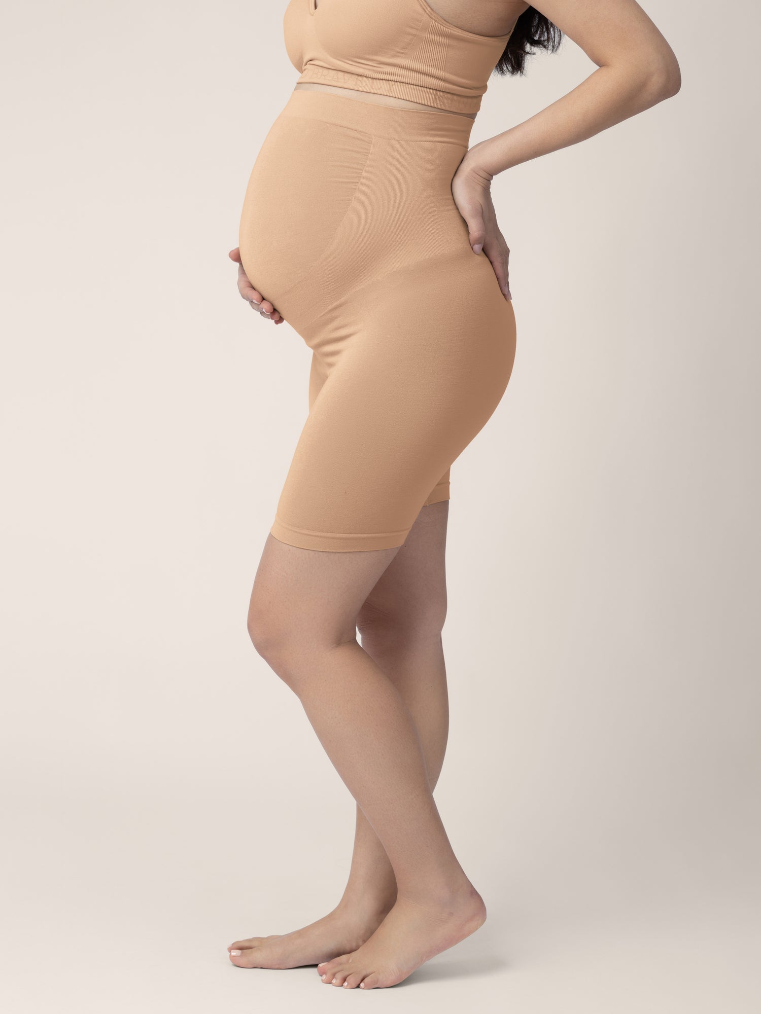 Pregnant model wearing the Seamless Bamboo Maternity Thigh Savers in Beige with her hand on her stomach and her back.
