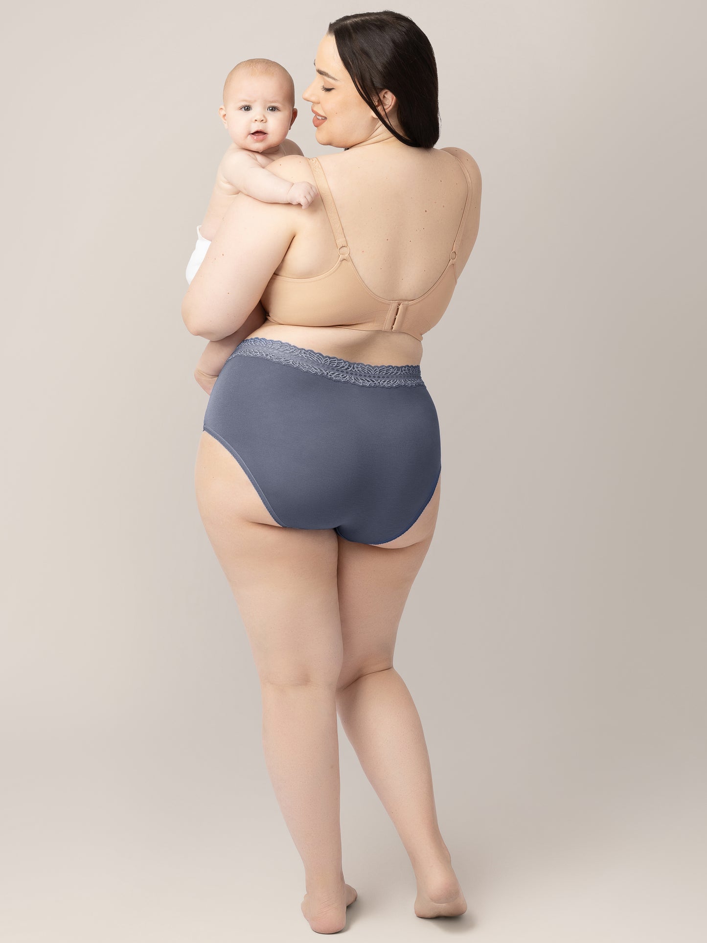 Back view of a model wearing the High Waisted Postpartum underwear in Dusty Hues holding her baby on her hip. 