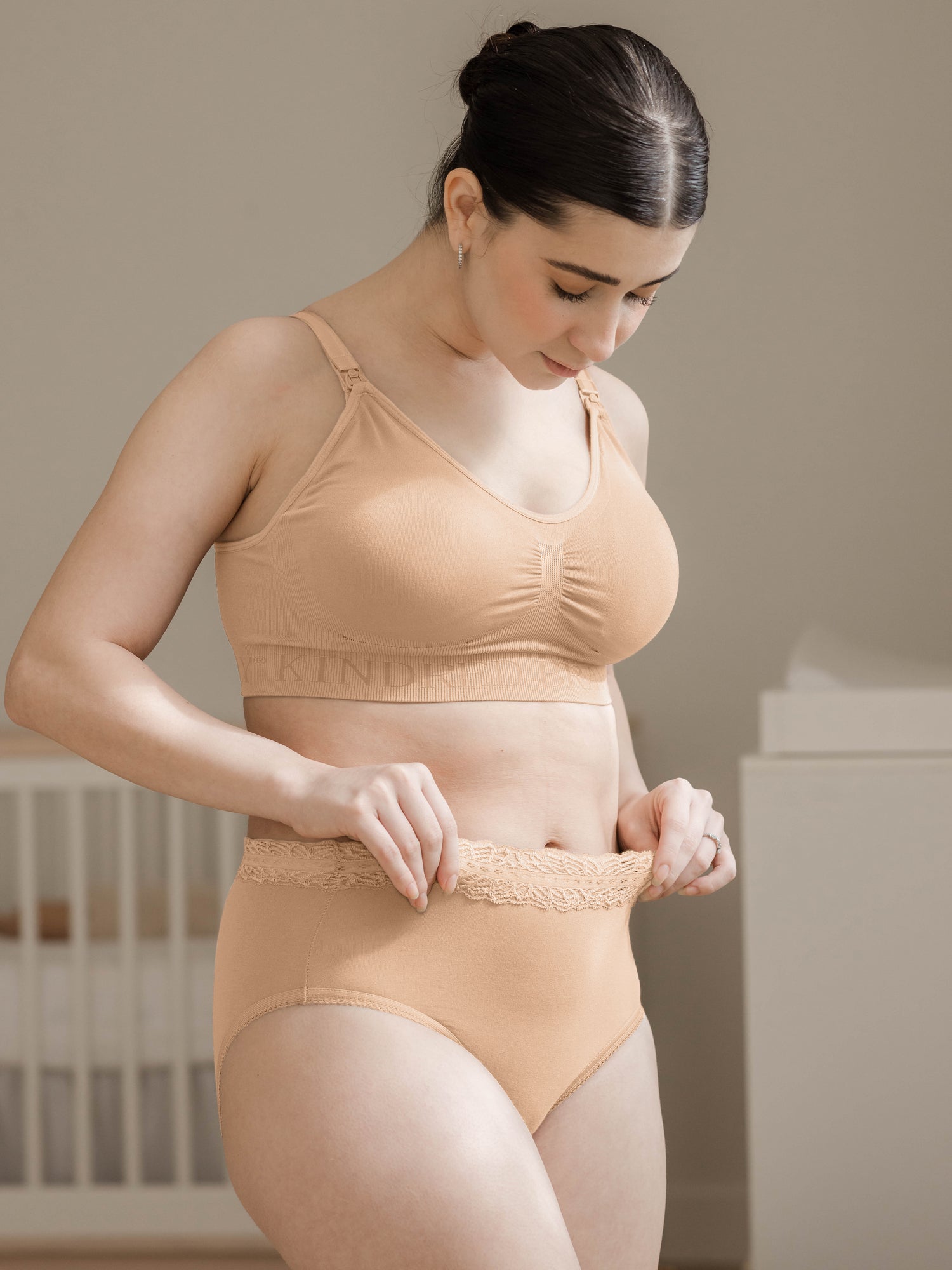 Model wearing the High-Waisted Postpartum Underwear in Assorted Neutrals looking down at the comfortable waistband. @model_info:Kianna is wearing a Small. 