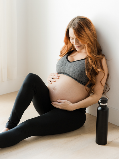 Pregnant model sitting on the ground holding her belly while wearing the Louisa Maternity & Postpartum Legging in Black. 