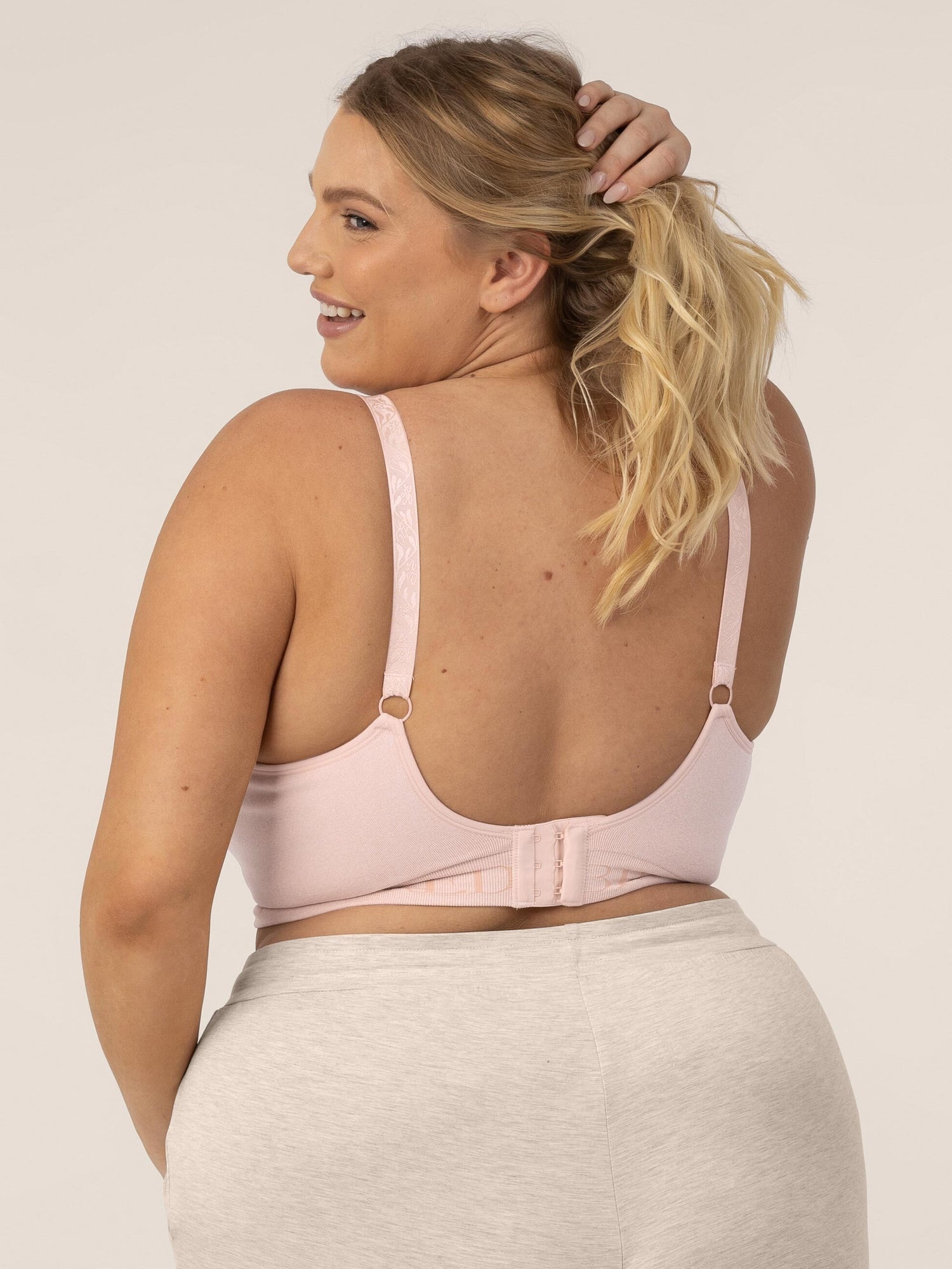 Busty model looking over her shoulder and pulling her hair back wearing the Sublime® Hands-Free Pumping & Nursing Bra in Pink Heather
