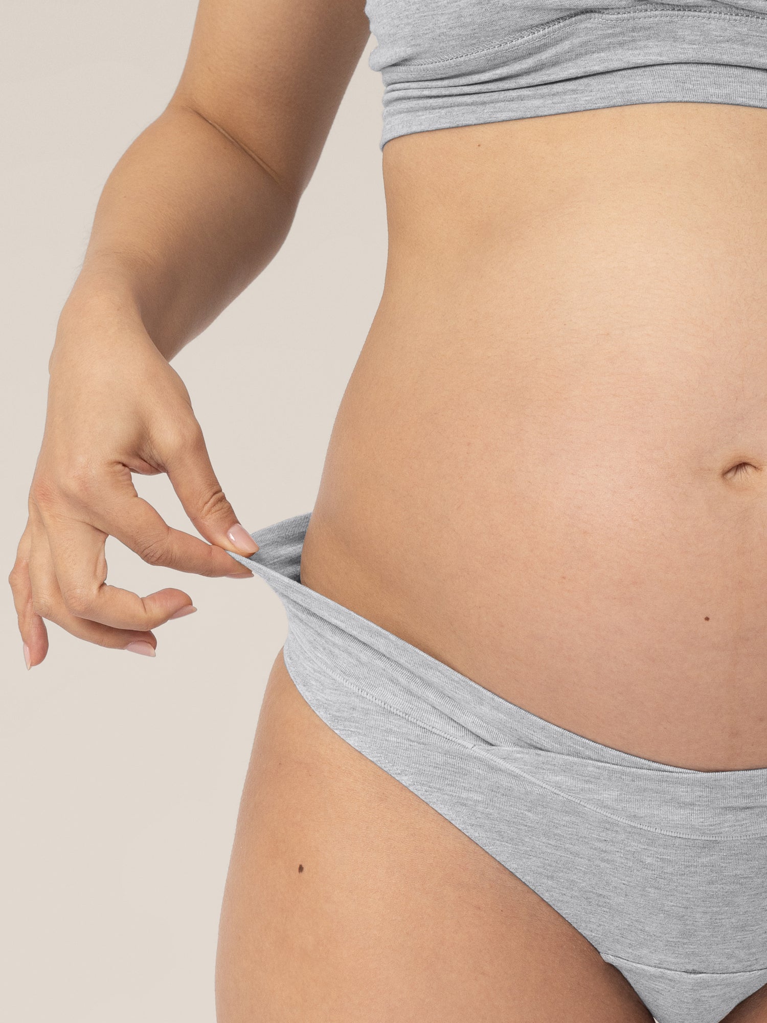 Closeup of a pregnant model holding onto the waistband of the Bamboo Maternity & Postpartum Thong in Grey Heather