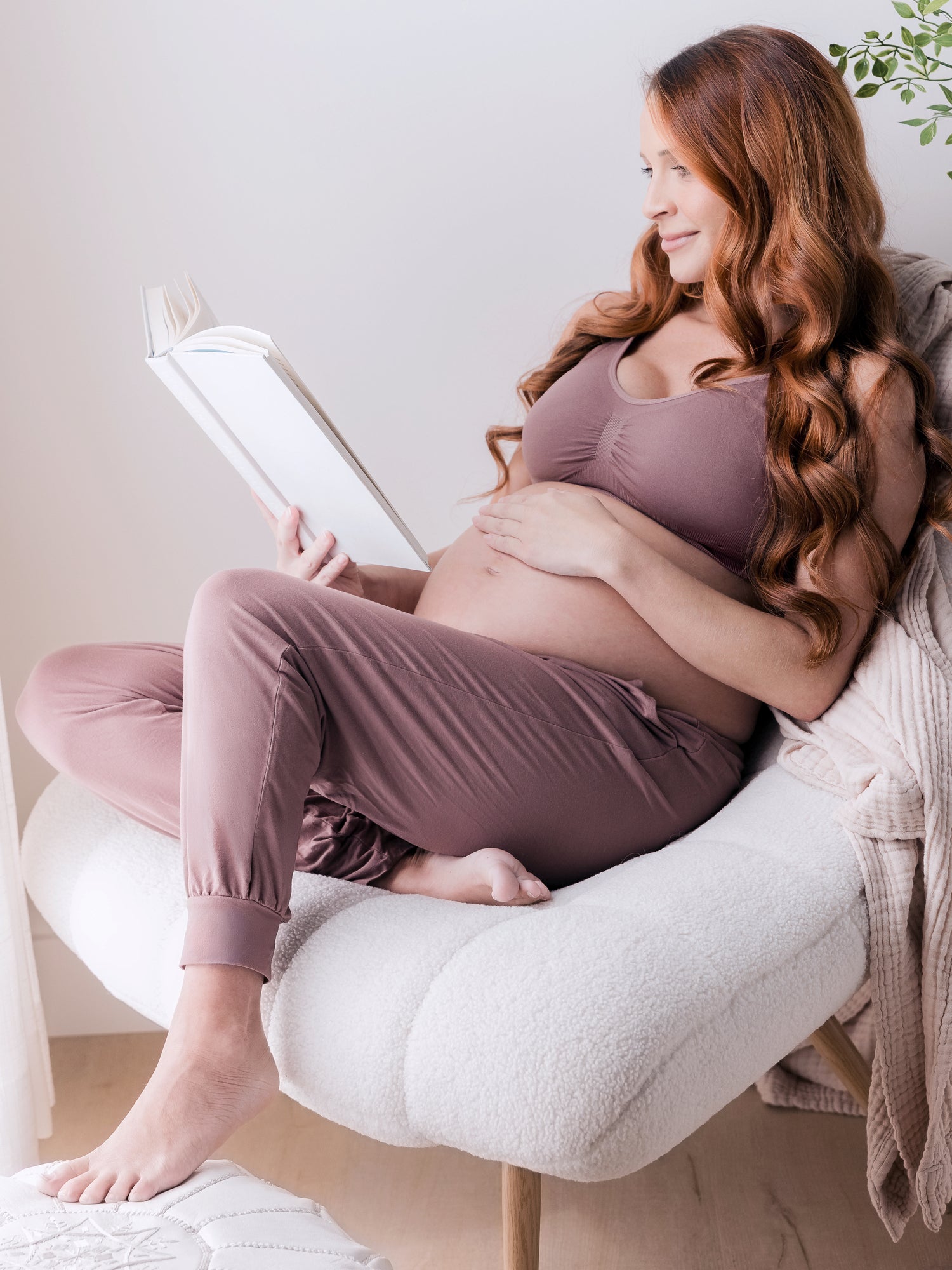 Pregnant model sitting in a chair reading while wearing Everyday Lounge Jogger in Twilight @model_info:Shannon is 5' and wearing a Small Regular. 