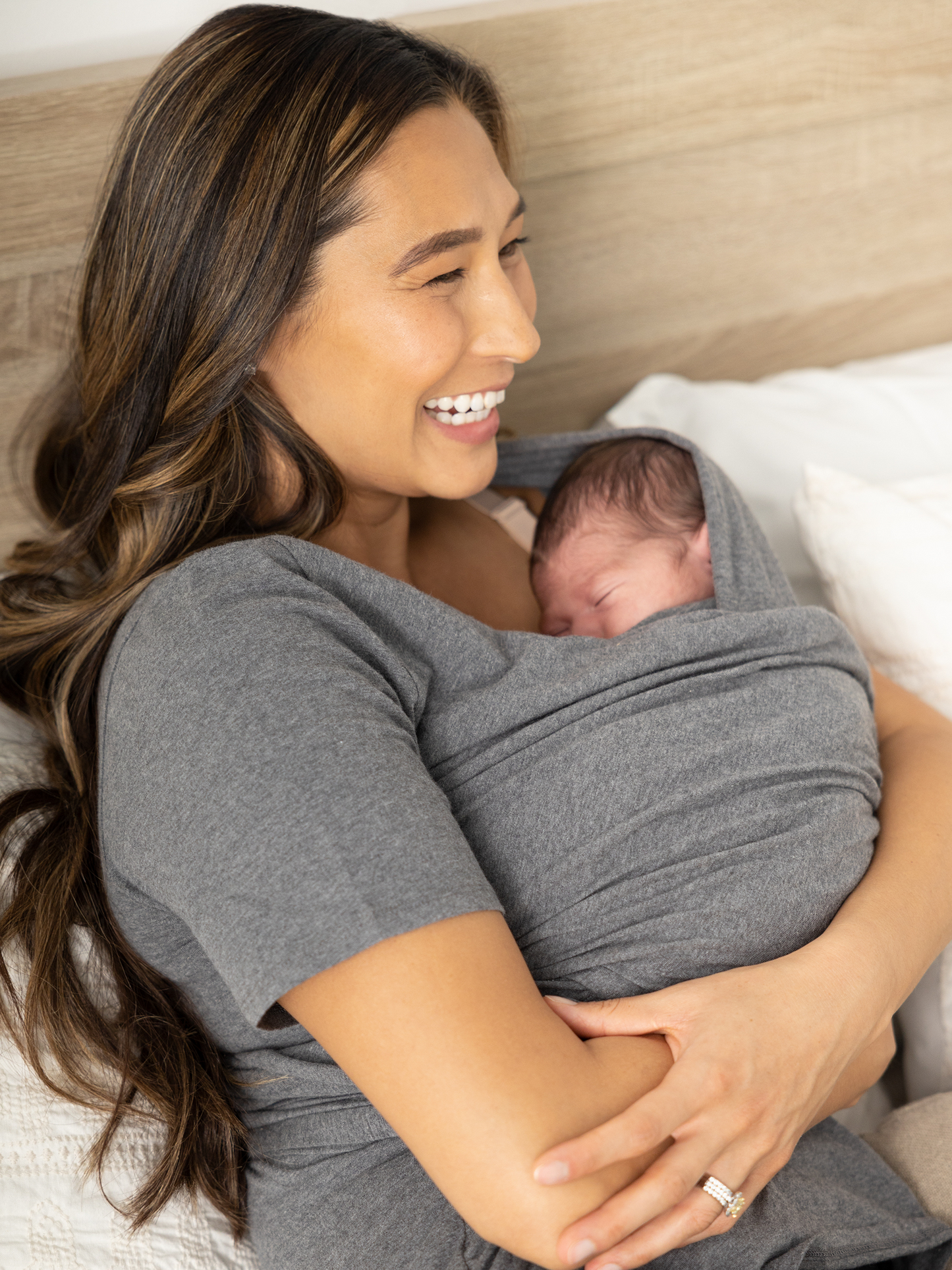 Model laying on a bed with her baby wearing the Organic Cotton Skin to Skin Wrap Top in Charcoal Grey Heather