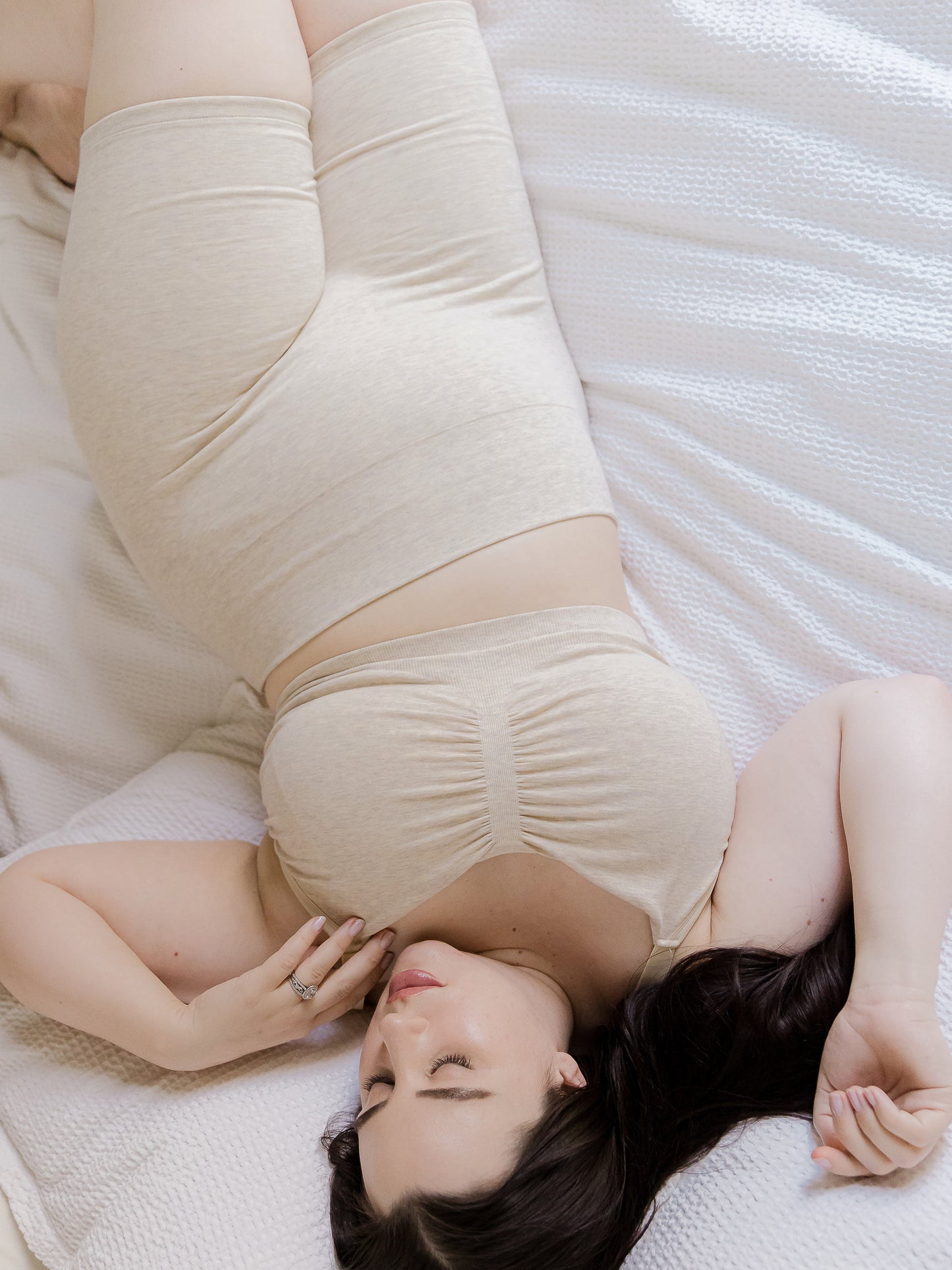 Model lounging on bed wearing the Sublime® Bamboo Maternity & Postpartum Bike Short in oatmeal heather, paired with matching Sublime® Bamboo Hands-Free Pumping Lounge & Sleep Bra