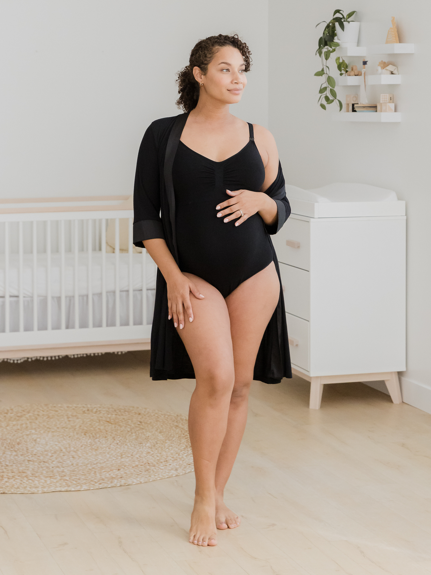 Pregnant model in nursery wearing the Sublime®️ Bamboo Maternity & Nursing Bodysuit, paired with the Emmaline Robe in black.  @model_info:Alysha is wearing a Large.