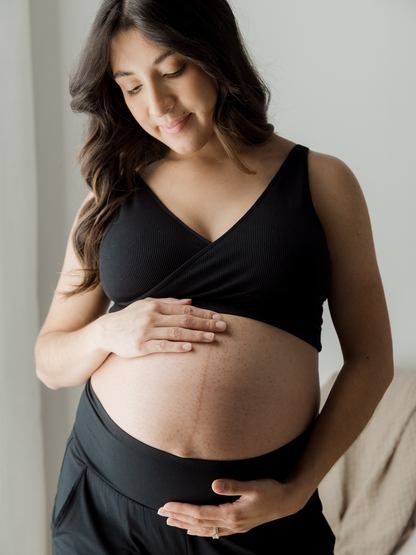 Pregnant model wearing the Sublime® Adjustable Crossover Nursing & Lounge Bra in Black holding her baby bump/