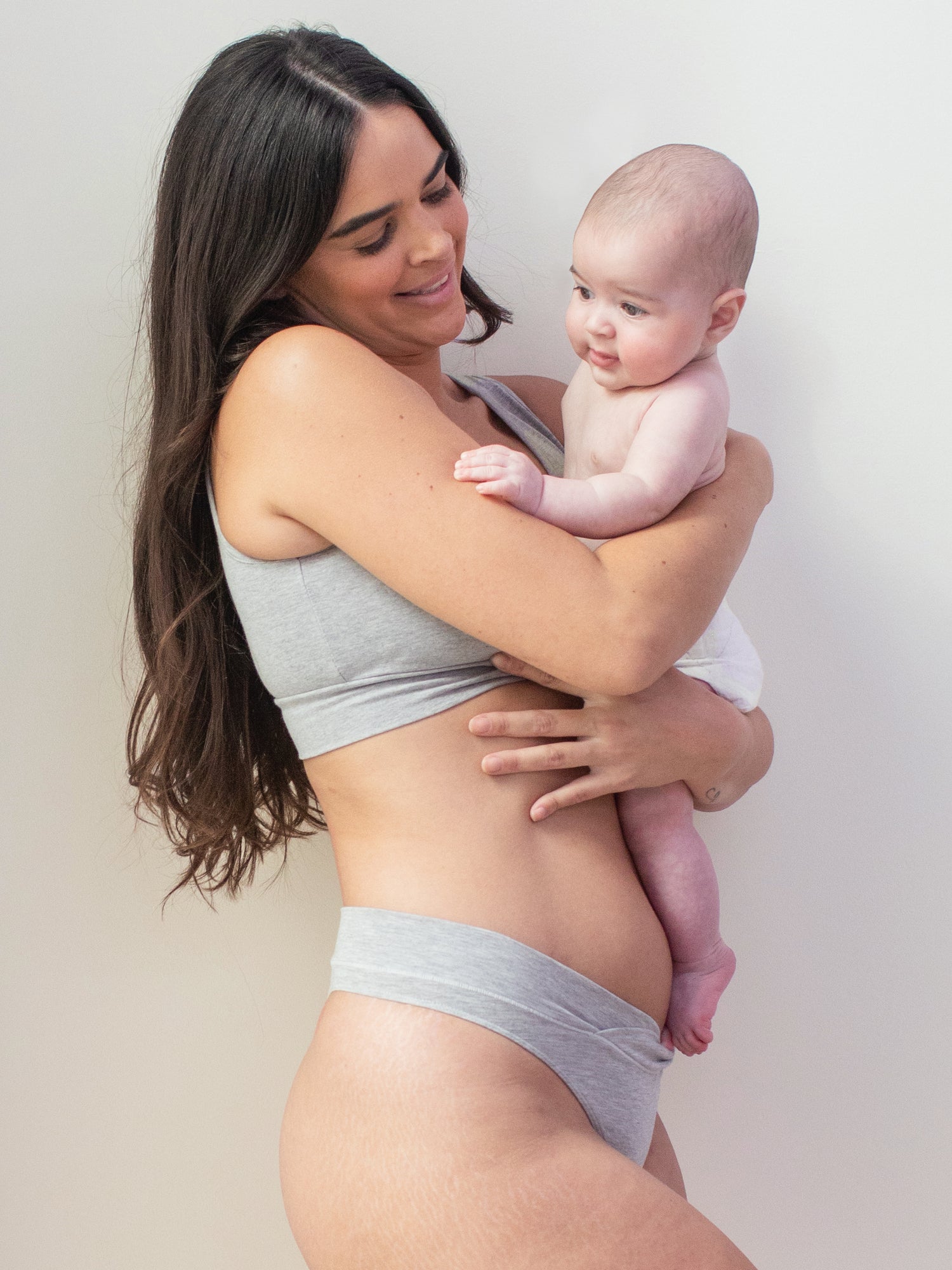 Model wearing the Bamboo Maternity & Postpartum Thong in Grey Heather holding her baby against her. 