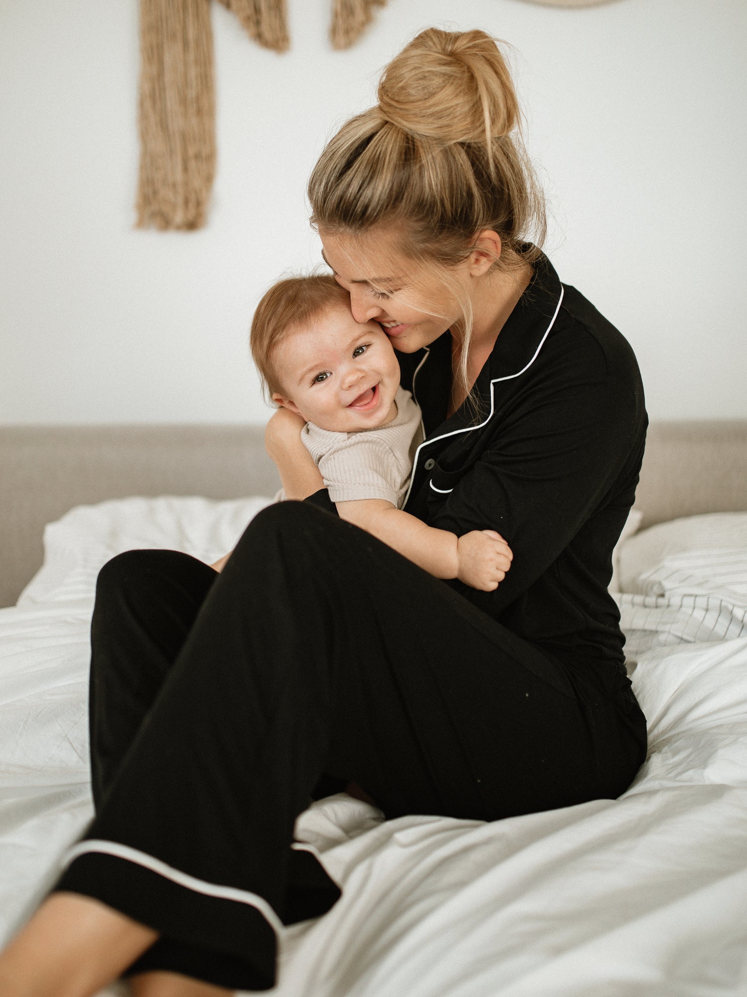 Model sitting on a bed with her baby wearing the Clea Bamboo Long Sleeve Pajama Set in Black