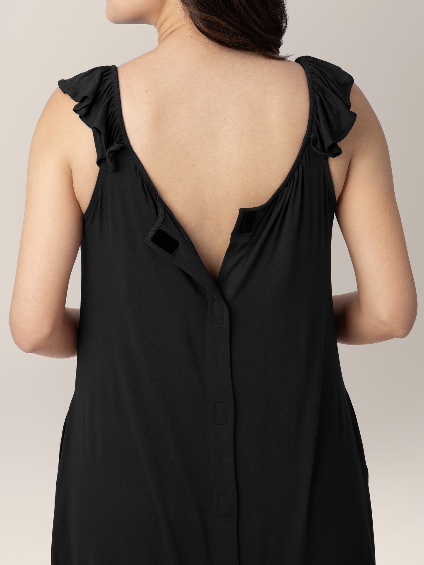 Closeup of the back of a pregnant model wearing the Ruffle Strap Labor & Delivery Gown in Black showing the easy velcro access.