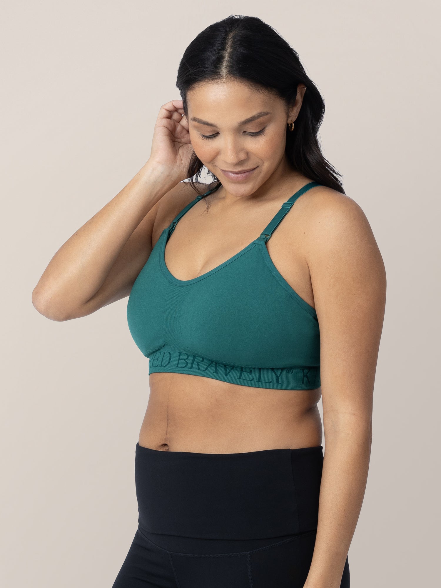 Model tucking her hair behind her ear while wearing the Sublime® Hands-Free Pumping & Nursing Sports Bra in teal.