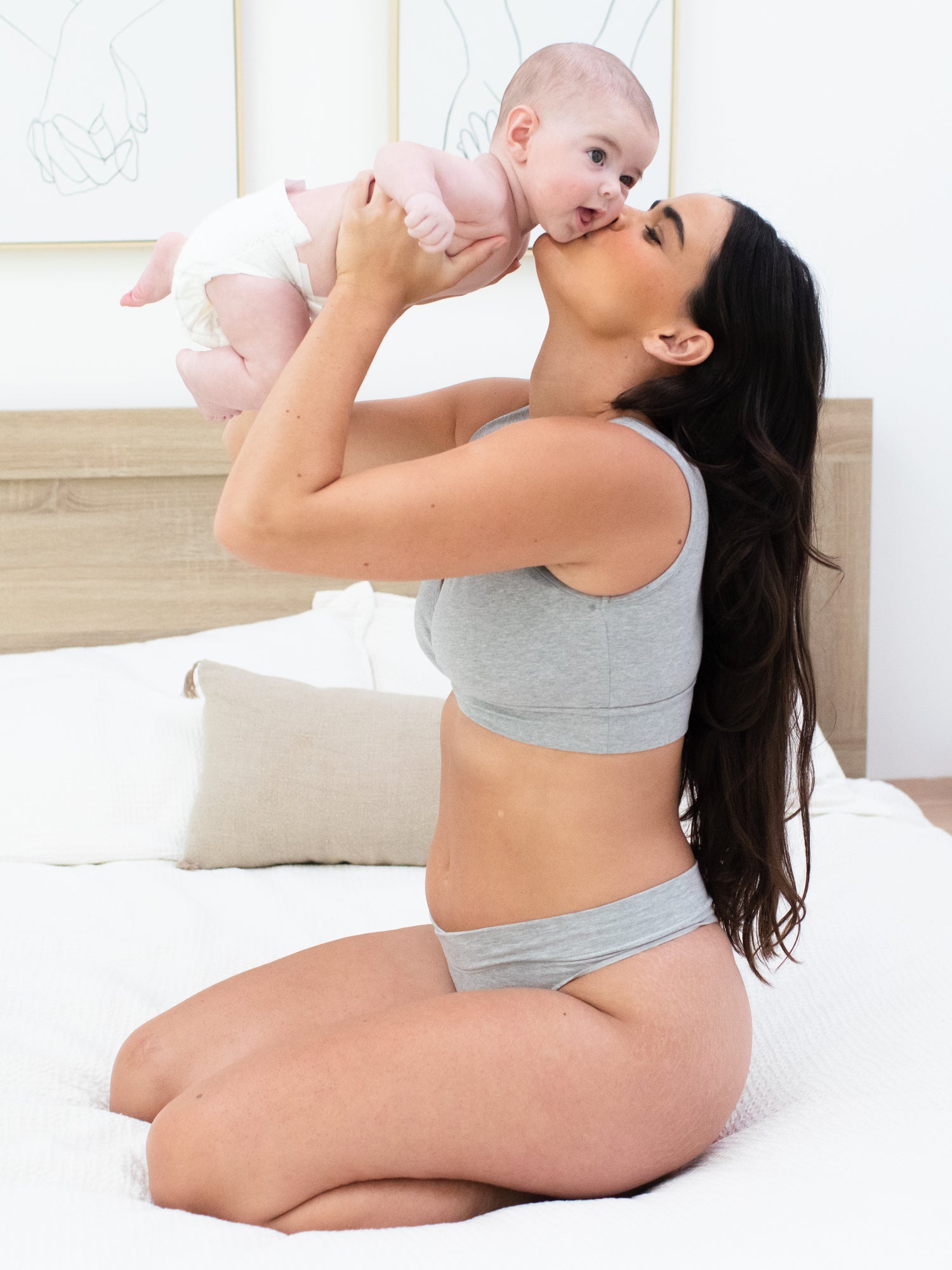 Model sitting on a bed holding her baby up in the air while wearing the Bamboo Maternity & Postpartum Thong in Grey Heather