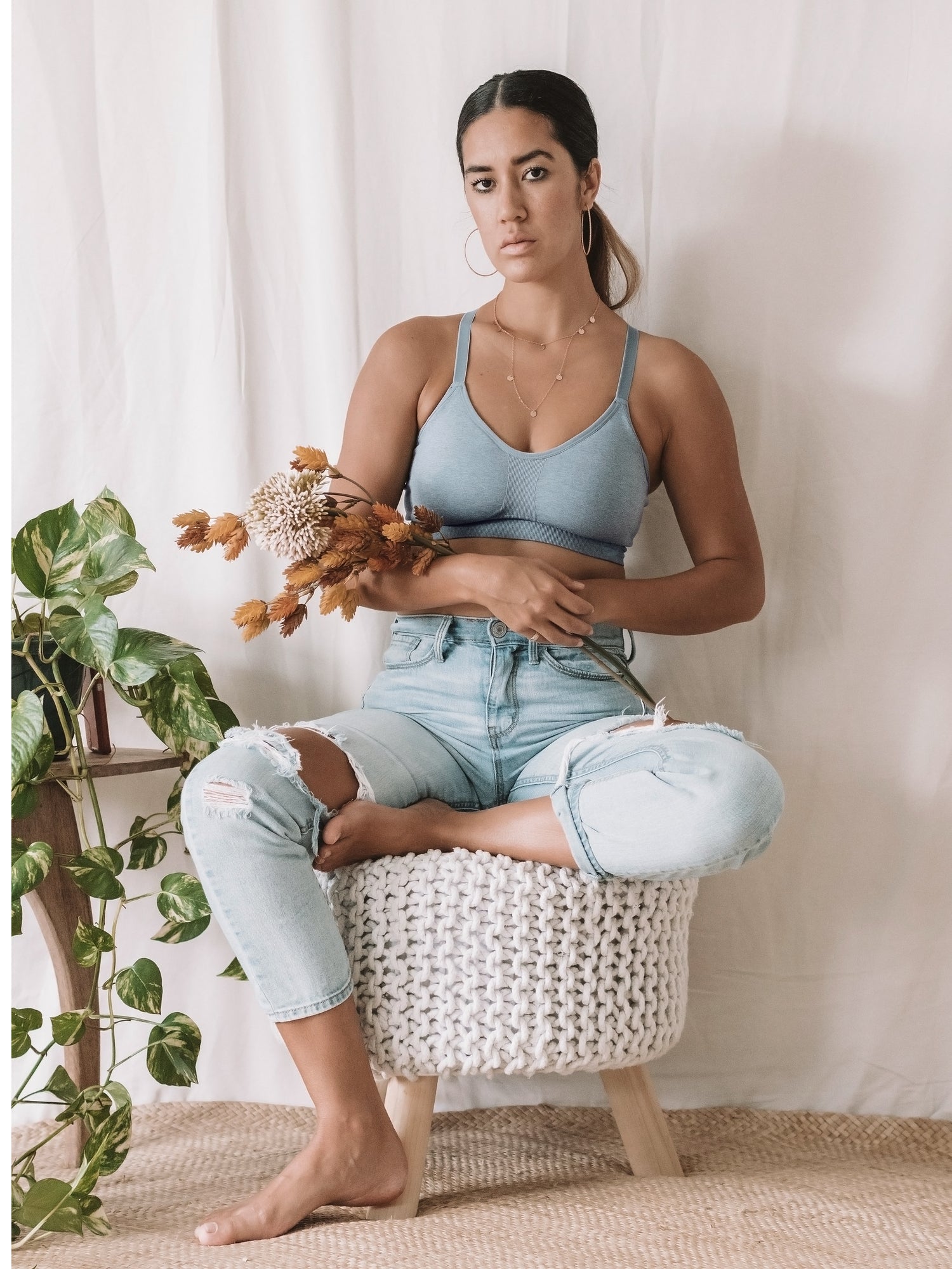 Model sitting on a small white knitted stool while wearing the Diana Sublime® Sports Bra in Seaglass Heather @model_info:Kiana is wearing a Small.