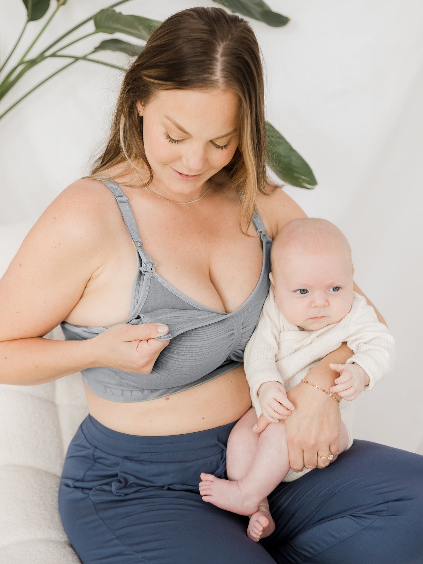 Model holding her baby while wearing the Sublime® Hands-Free Pumping & Nursing Bra in Grey