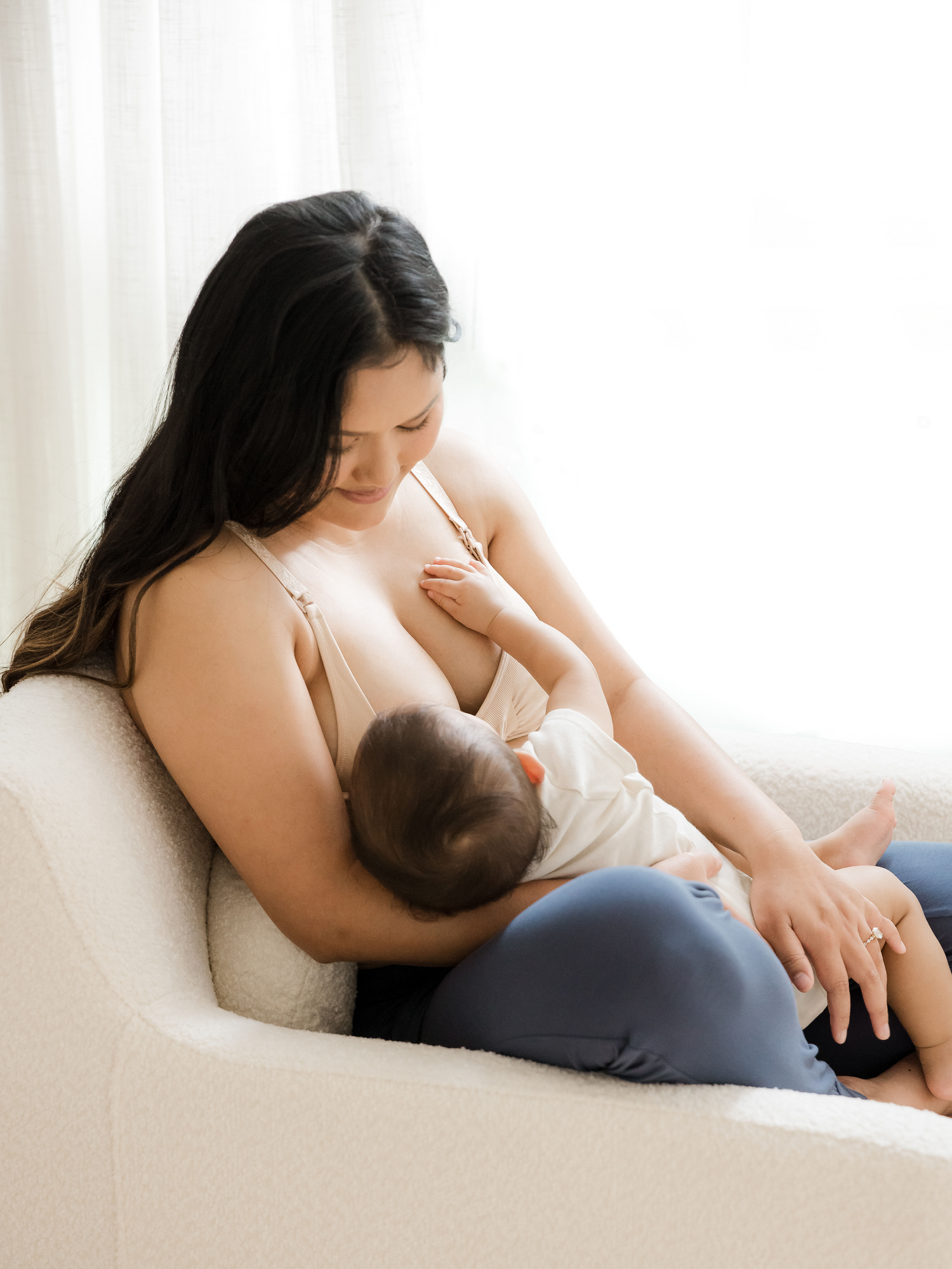 Model sitting in a chair wearing the Simply Sublime® Nursing Bra in Beige breastfeeding her baby. @model_info:Binc is wearing a Medium Busty.