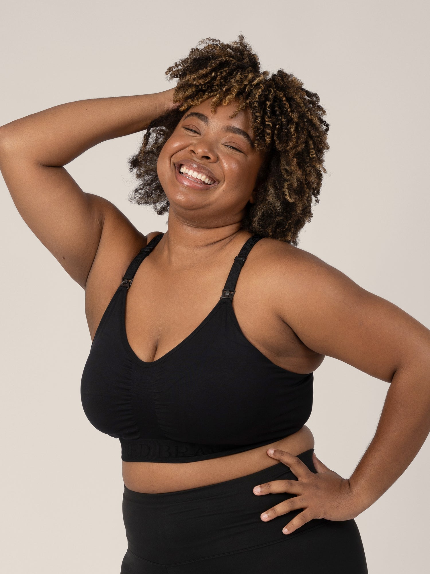 Model wearing the Sublime® Nursing Sports Bra in Black with one hand on her hip and the other in her hair.
