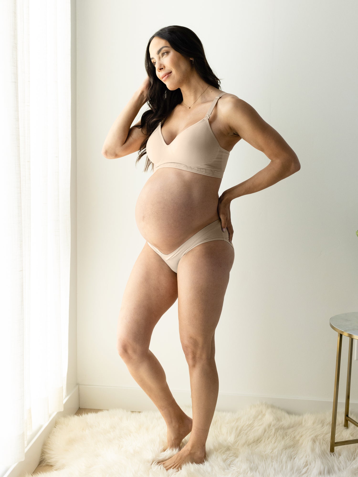 Pregnant model standing near a window wearing the Under-the-Bump Bikini Underwear in assorted colors 