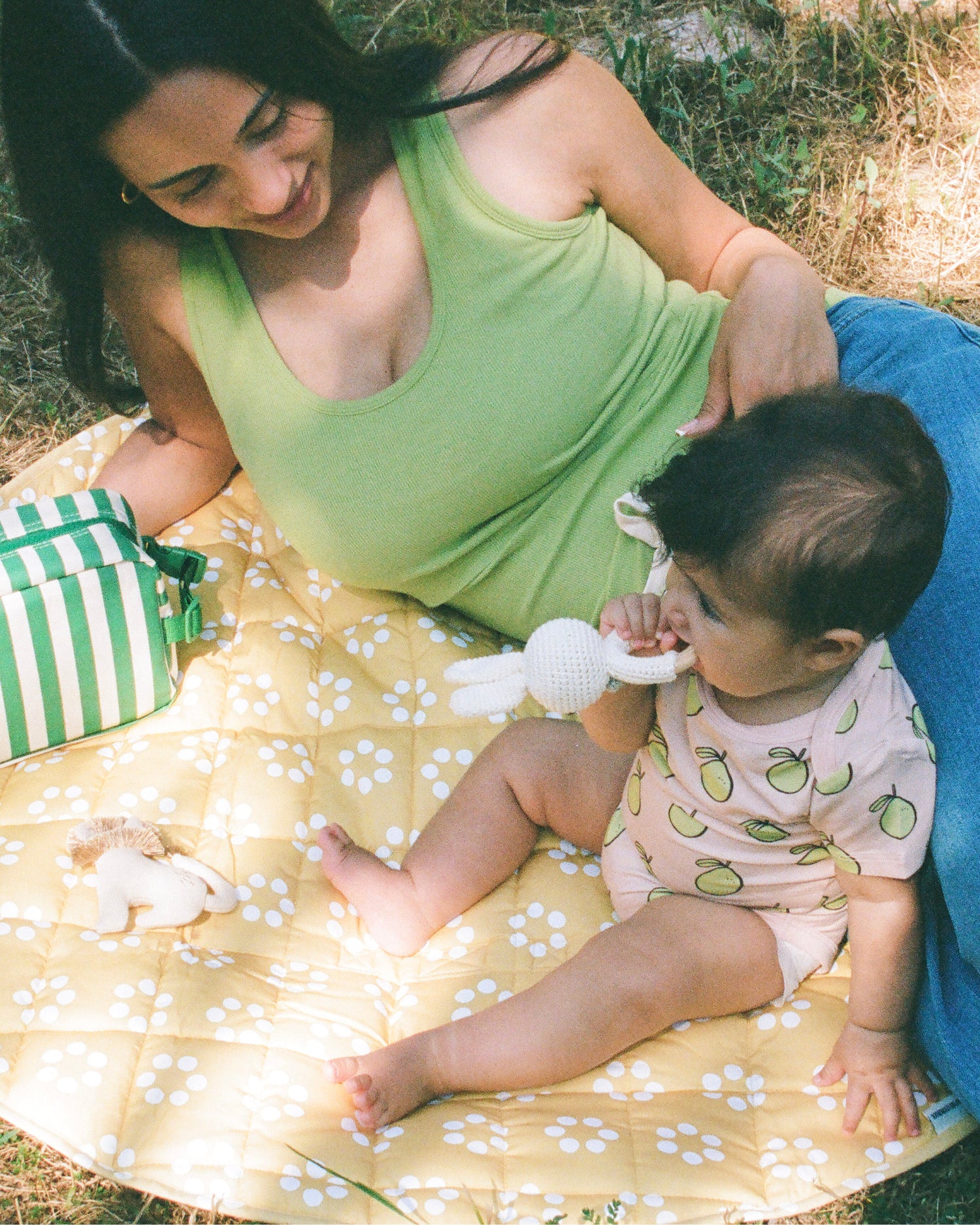 Mom laying on Inside/Outside Play Mat in Sunshine Dots and wearing Ribbed Bamboo Scoop Neck Nursing Tank in Avocado next to baby wearing Bamboo Short Sleeve & Shorts Set in Pink Pomelo on a grassy patch. Next to mom is Mini Cooler Bag in Green Stripe.@model_info:Zoe is wearing a Small.