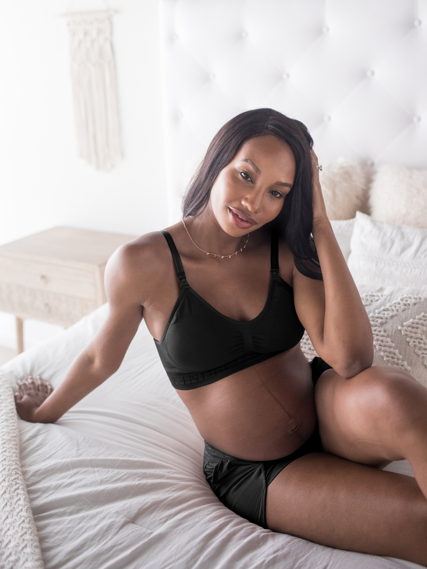 Pregnant model sitting on a bed while wearing the Simply Sublime® Nursing Bra in Black
