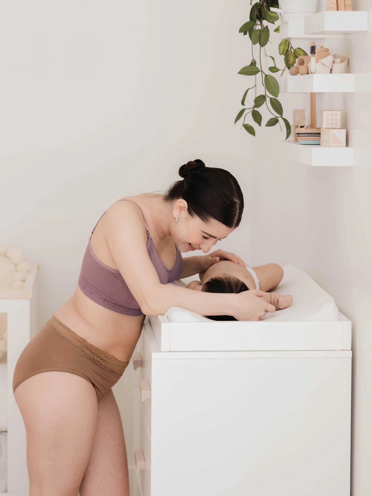 Model wearing the High Waisted Postpartum underwear in Dusty Hues while changing her baby on a changing table. 