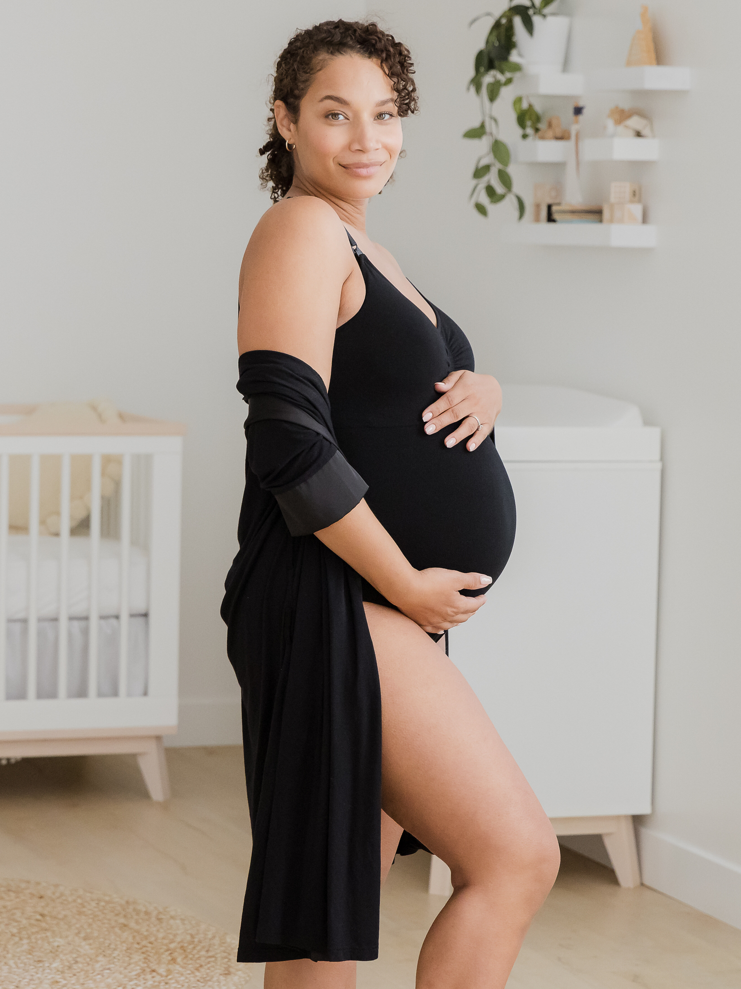 Side view of pregnant model in nursery wearing the Sublime®️ Bamboo Maternity & Nursing Bodysuit, paired with the Emmaline Robe in black.