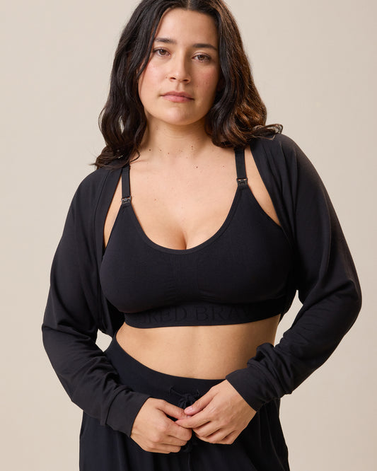 Woman wearing the French Terry Cardigan Shrug in black with matching Sublime Nursing Sports Bra against a beige background@model_info:Linda is wearing an XS/S.