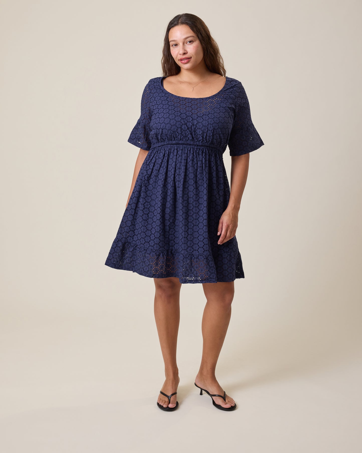 Woman wearing the Dahlia Eyelet Maternity & Nursing Dress in Navy on a beige background@model_info:Alana is 5'7" and wearing a Large.
