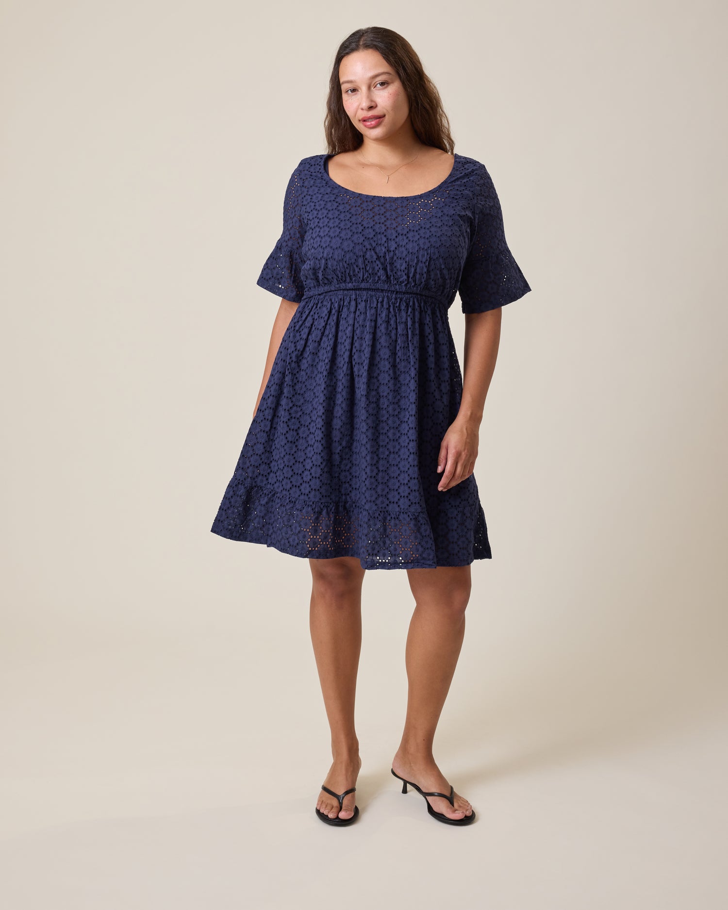 Woman wearing the Dahlia Eyelet Maternity & Nursing Dress in Navy on a beige background@model_info:Alana is 5'7" and wearing a Large.
