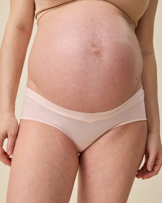 Close up of model wearing Grow with Me™ Maternity & Postpartum Hipster in Soft Pink on a beige background@model_info:Tassia is wearing a Medium.
