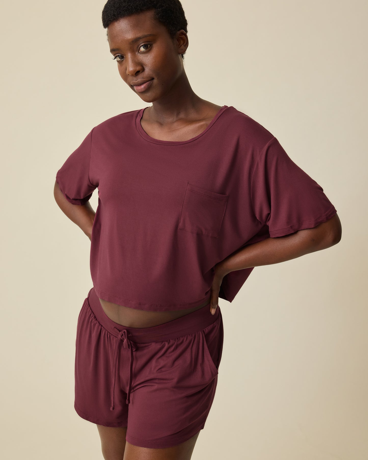 Model is wearing Aria Bamboo Casual Cropped Short Sleeve Top in Deep Burgundy and Aria Bamboo Casual Lounge Short in Deep Burgundy, on a beige background. @model_info:Anna is wearing a Small.