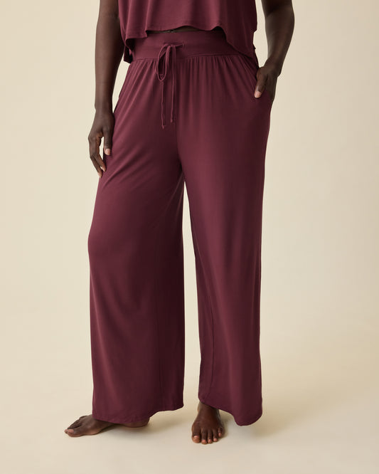 Model is wearing Aria Bamboo Cropped V-neck Tank in Deep Burgundy and Aria Bamboo Casual Lounge Pant in Deep Burgundy on a beige background.@model_info:Anna is 5'8.5" and wearing a Medium