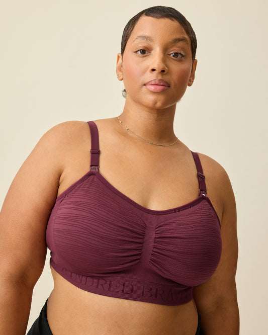 Model is wearing Sublime® Hands-Free Pumping & Nursing Bra in Deep Burgundy, on a beige background. @model_info:Brittany is wearing an X-Large.