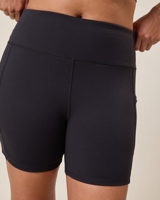Stevie Active Postpartum Bike Short in black worn by a person on a beige background@model_info:Alana is 5'7" and wearing a Large.