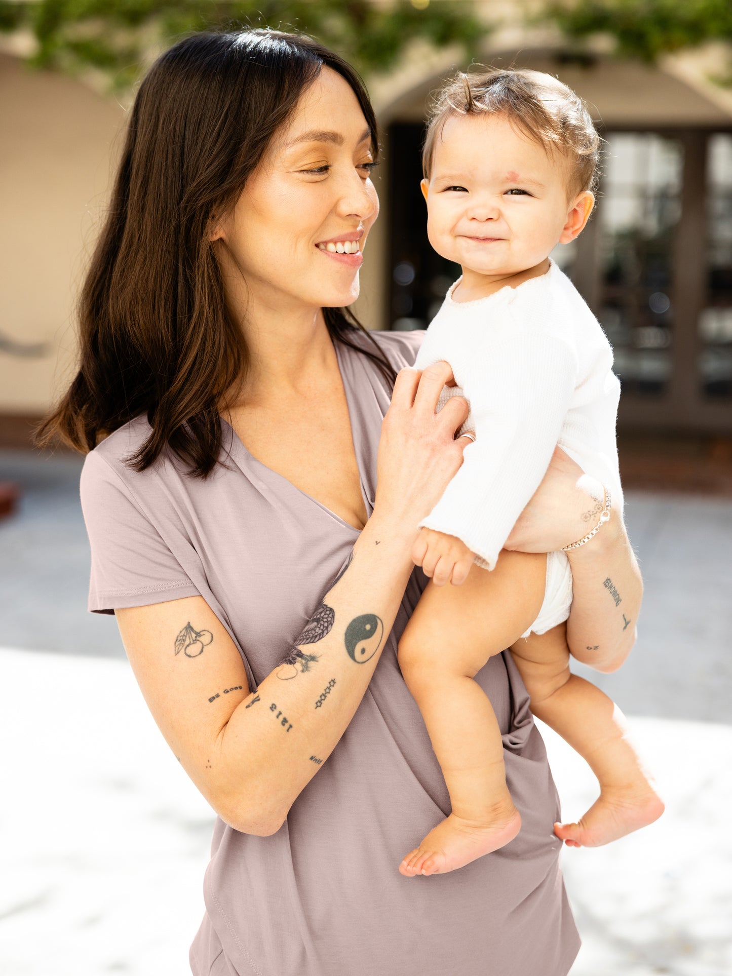 Model outside holding baby and wearing the Bamboo Draped Nursing Top in lilac stone