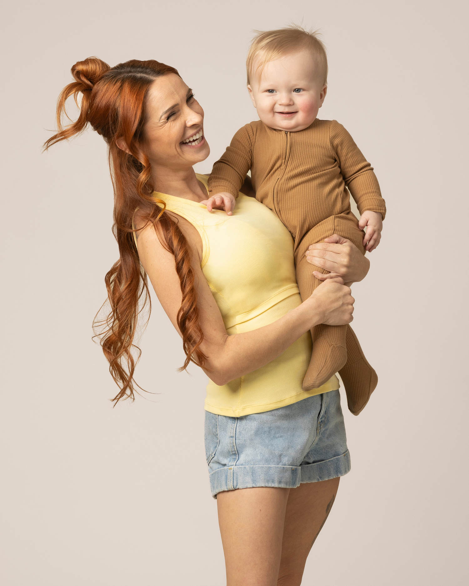 Model holding baby wearing the Ribbed Bamboo Racerback Nursing Tank in Butter Yellow, paired with denim shorts