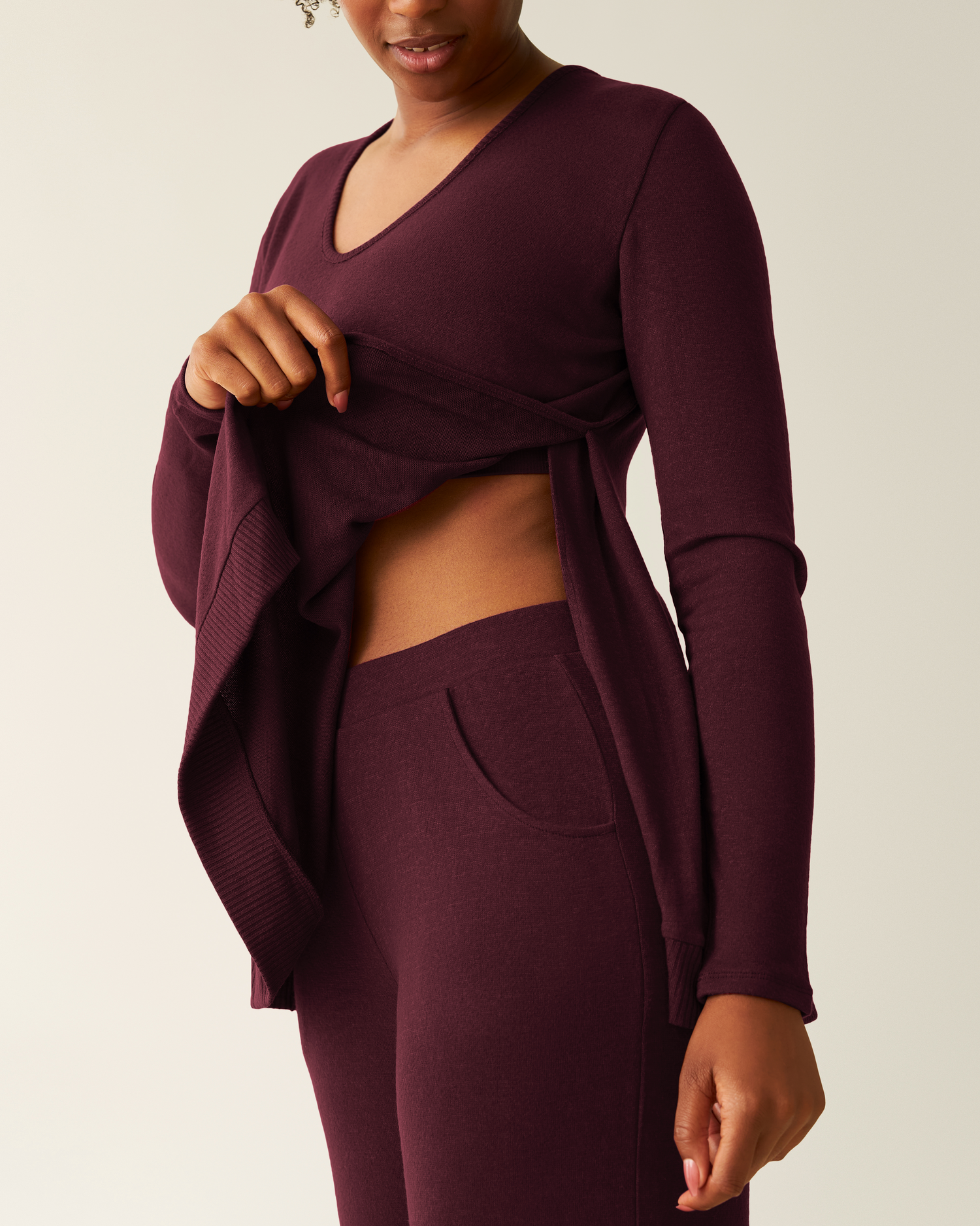 Person showing side opening of the CozyKnit Maternity & Nursing V-neck Top in Deep Burgundy with matching pants on a plain background