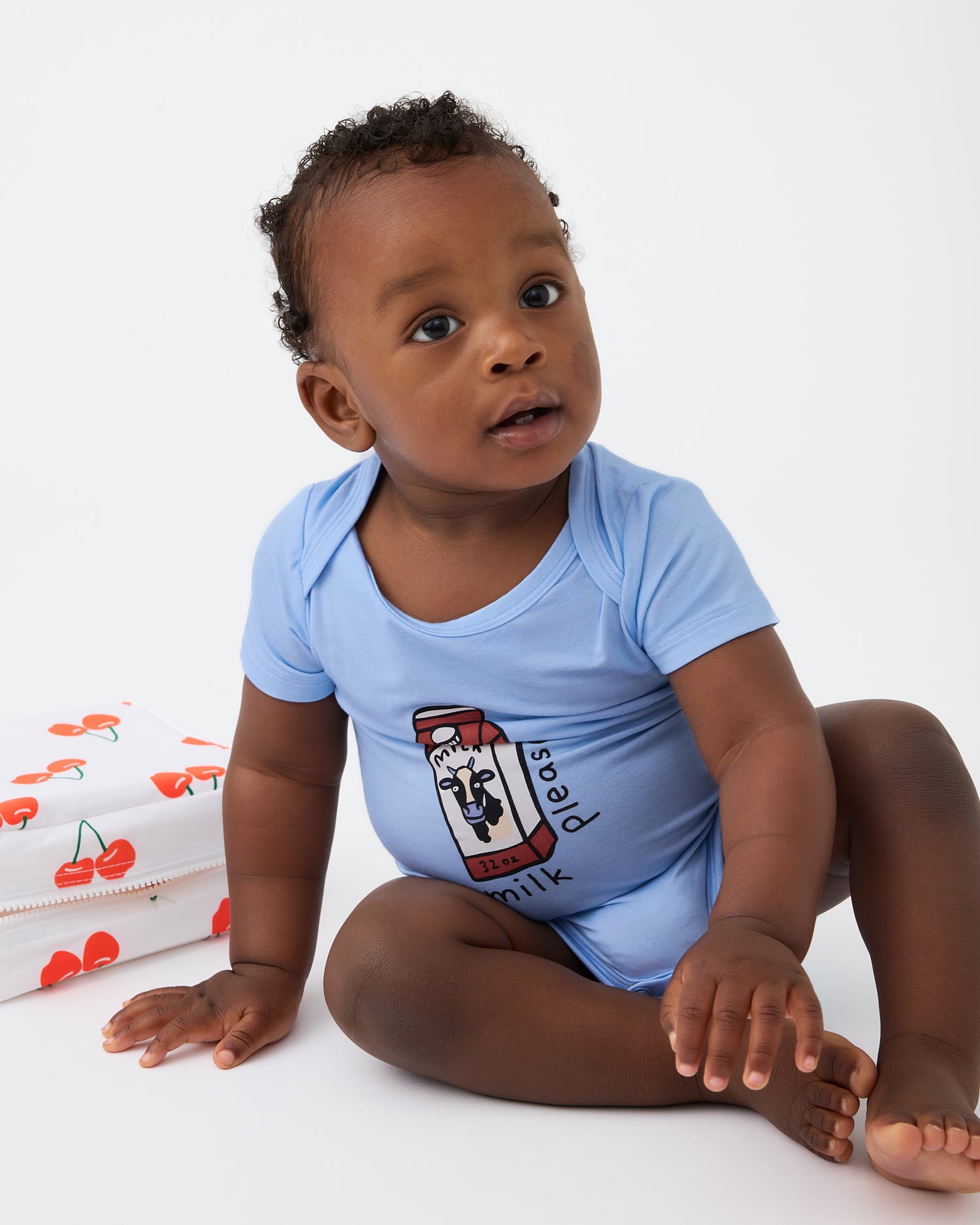 Baby is playing with bag and wearing Baby Onesie Two-Pack in Milk Please on a beige background@model_info:Jobadaiah is wearing 6-12 months.