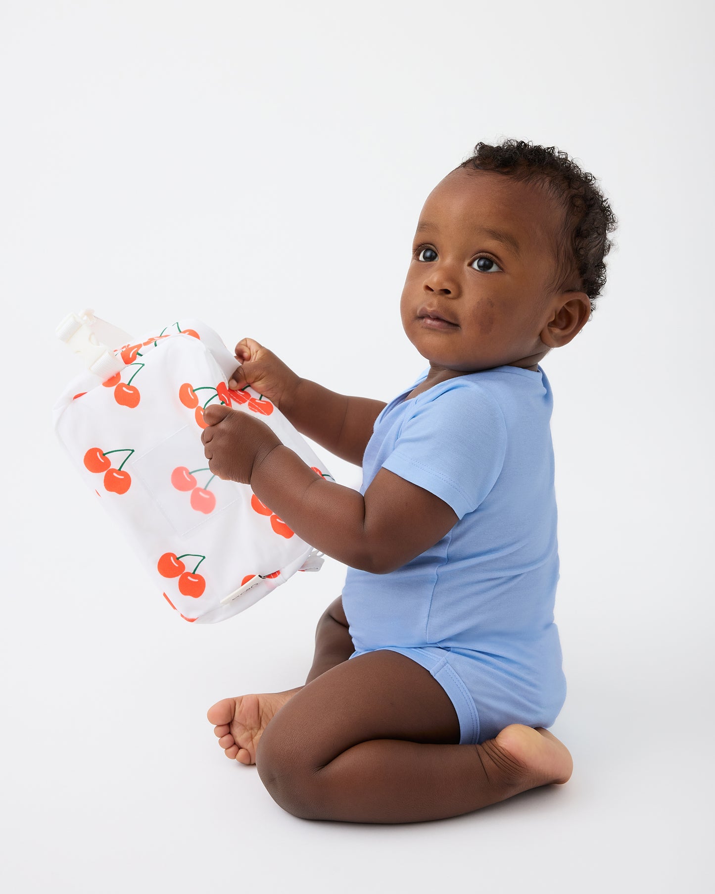 Baby is playing with bag and wearing Baby Onesie Two-Pack in Milk Please on a beige background