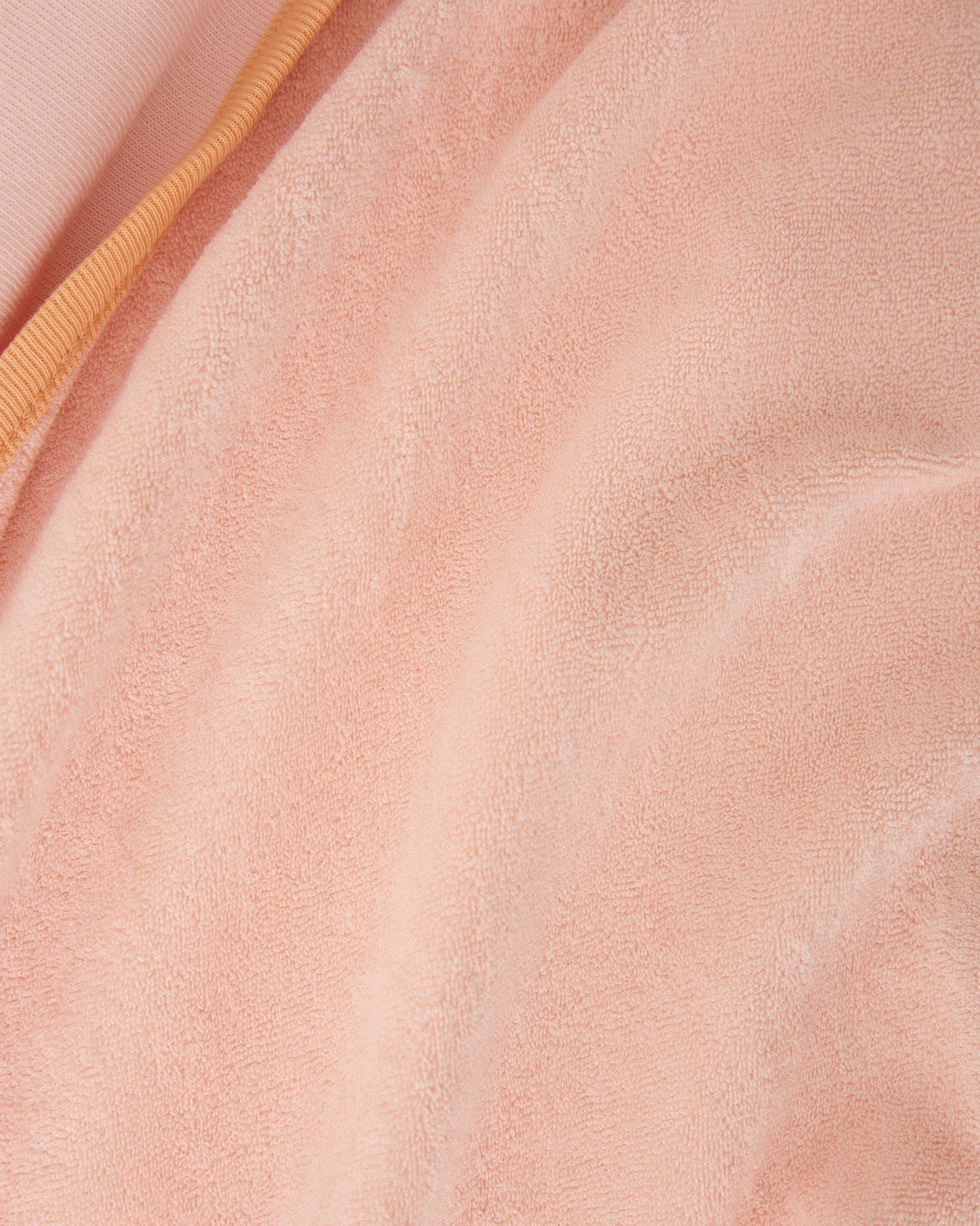 Close up of soft towel texture on Toddler Poncho Towel in Peach Whip on a beige background