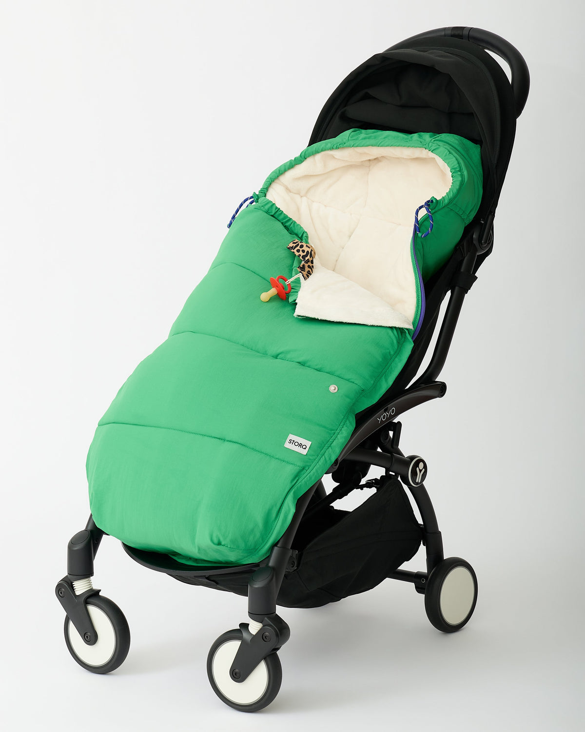 Cozy Stroller Footmuff in Green secured into a black stroller with a Pacifier Clip in Leopard attached, on an off white background.