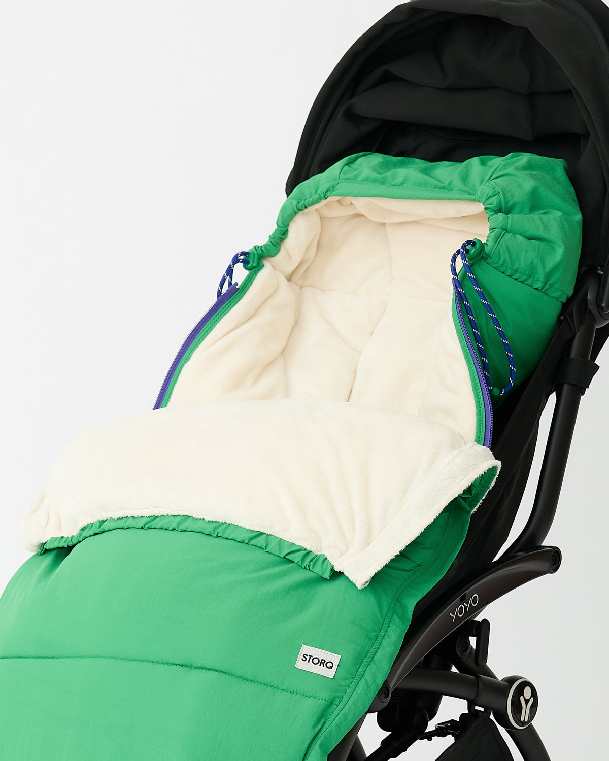 Cozy Stroller Footmuff in Green secured into a black stroller with front zipped down to see fuzzy interior, on an off white background.