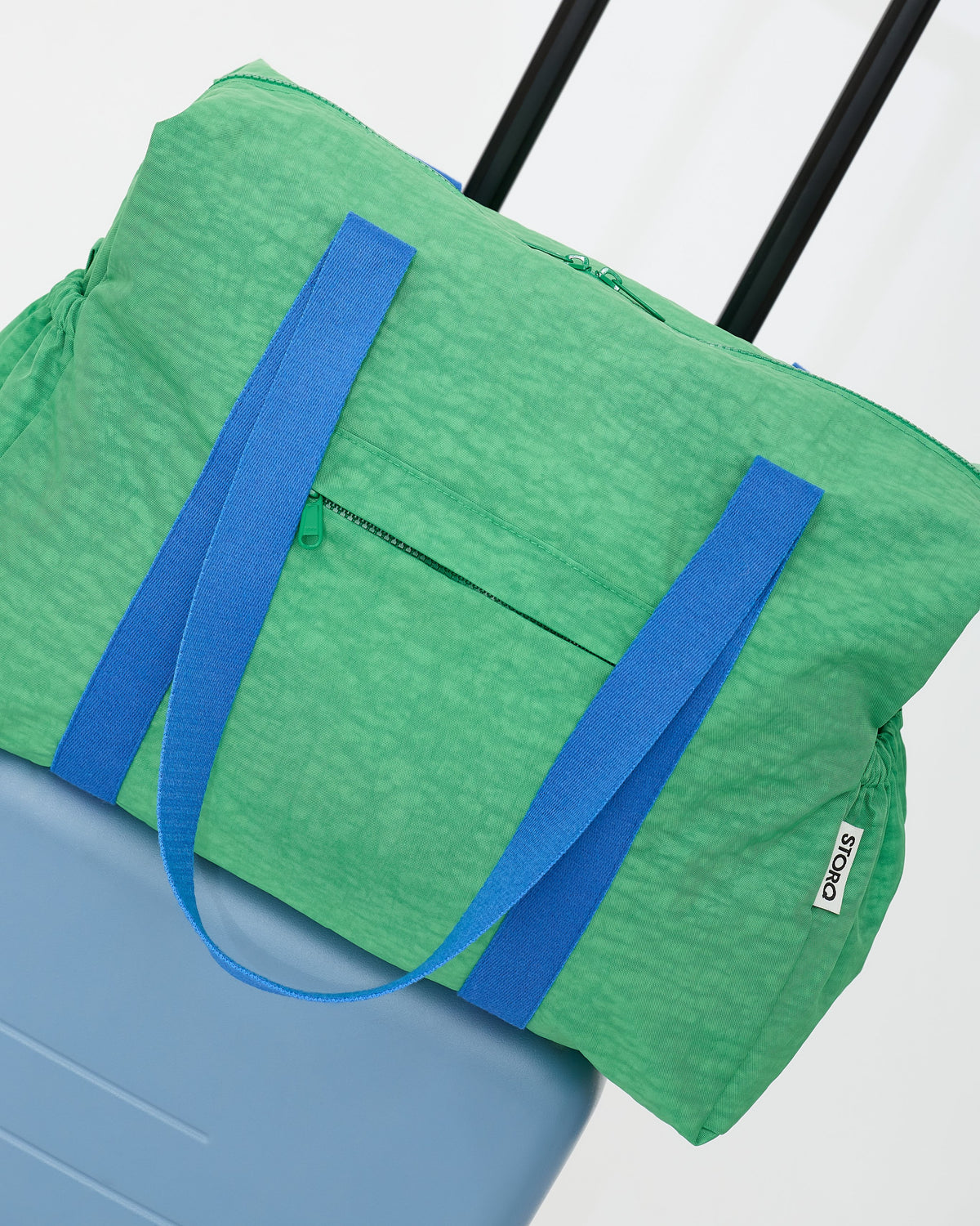 The Large Weekender Bag in Green stacked on top of a suitcase on an off white background.