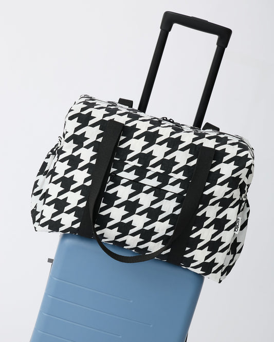 Large Weekender Bag in Black Houndstooth is set ontop of a suitcase on an off white background.