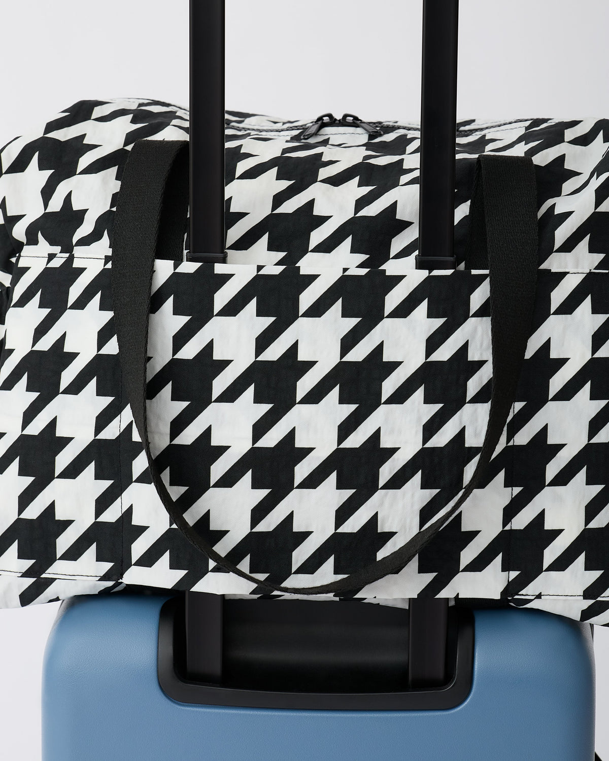 Large Weekender Bag in Black Houndstooth is set ontop of a suitcase on an off white background.